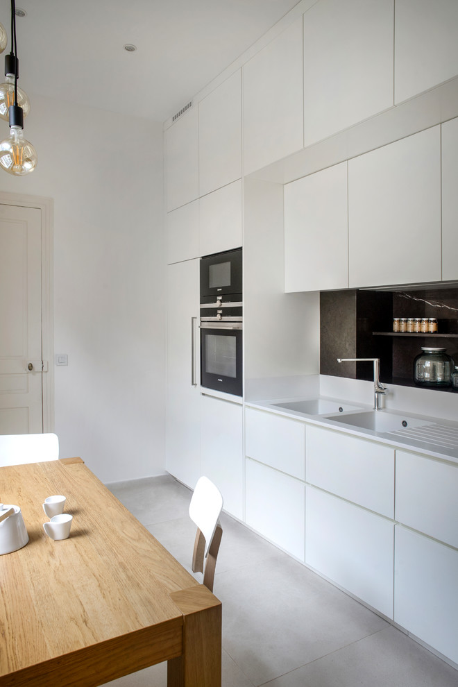 Immagine di una cucina lineare minimal con lavello a doppia vasca, ante con riquadro incassato, ante bianche, paraspruzzi bianco, elettrodomestici da incasso, pavimento grigio e top bianco