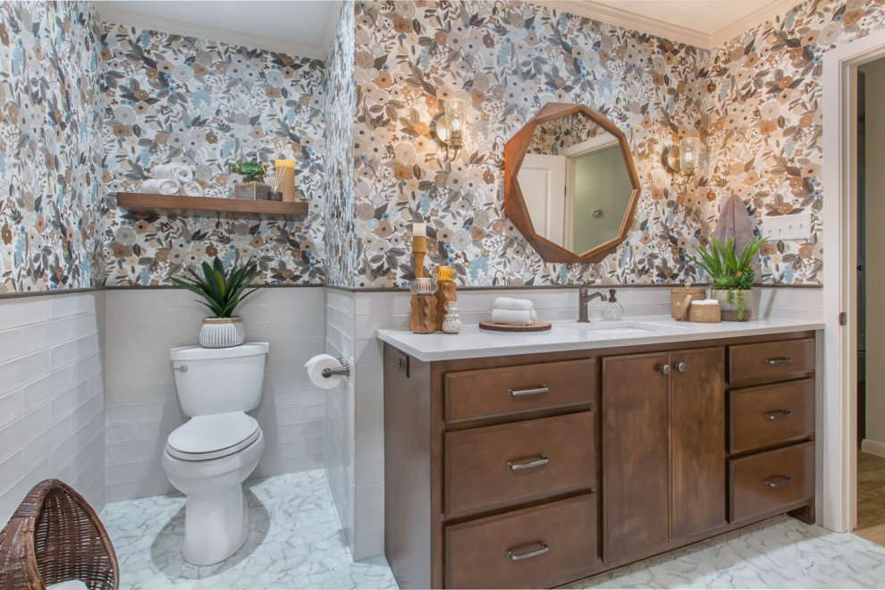 Photo of a mid-sized transitional 3/4 bathroom in Other with raised-panel cabinets, brown cabinets, an alcove tub, an alcove shower, a two-piece toilet, white tile, glass tile, multi-coloured walls, mosaic tile floors, an undermount sink, quartzite benchtops, grey floor, a shower curtain, white benchtops, a single vanity, a built-in vanity and wallpaper.