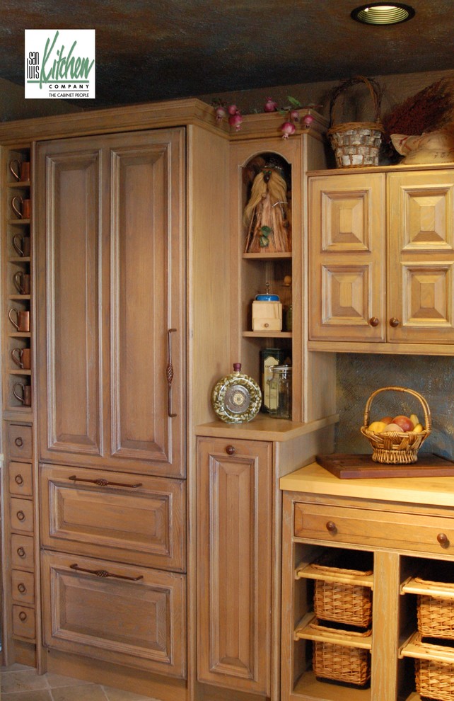 Example of a tuscan l-shaped open concept kitchen design in San Luis Obispo with an undermount sink, distressed cabinets, wood countertops and paneled appliances