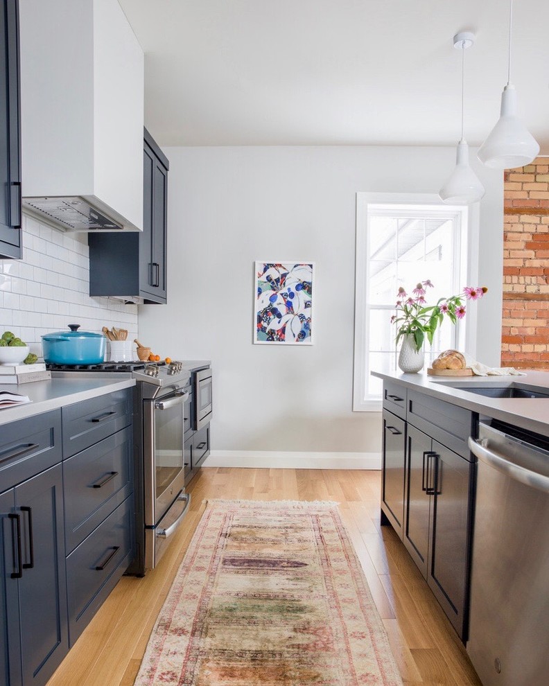 Mid-sized transitional single-wall kitchen in Toronto with an undermount sink, shaker cabinets, blue cabinets, solid surface benchtops, white splashback, subway tile splashback, stainless steel appliances, light hardwood floors, with island, beige floor and grey benchtop.