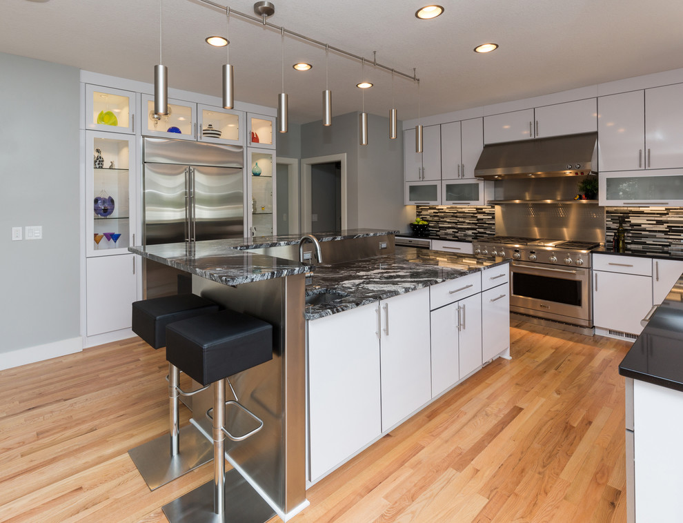 Large trendy u-shaped light wood floor open concept kitchen photo with an undermount sink, flat-panel cabinets, white cabinets, granite countertops, multicolored backsplash, mosaic tile backsplash, stainless steel appliances and an island