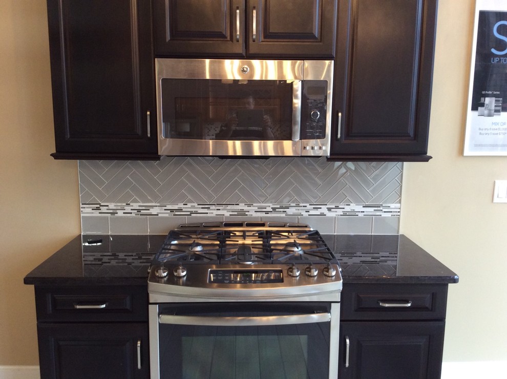 Example of a small minimalist single-wall porcelain tile home design design with raised-panel cabinets, dark wood cabinets, granite countertops, gray backsplash, glass tile backsplash, stainless steel appliances and no island