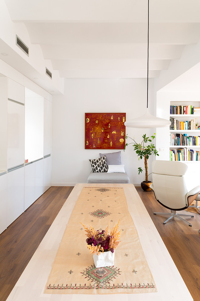 This is an example of a mid-sized contemporary open concept family room in Barcelona with a library, white walls, medium hardwood floors, no tv and brown floor.