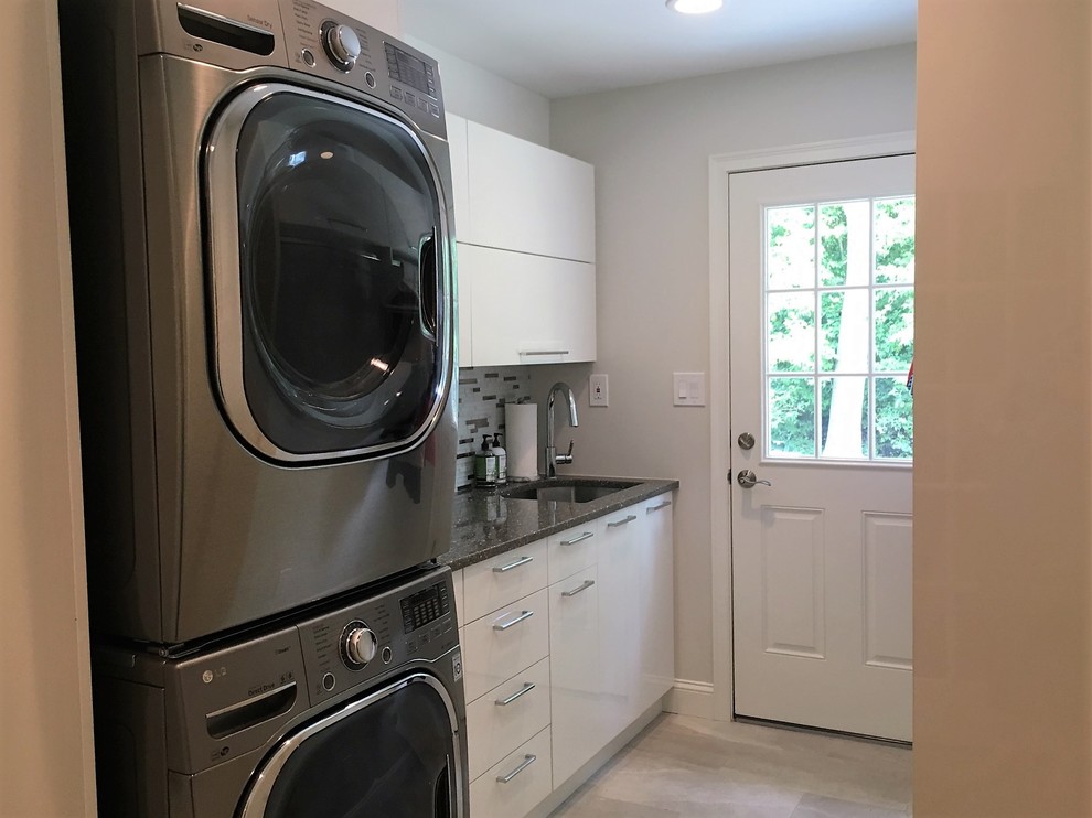 Inspiration for a small transitional single-wall dedicated laundry room in Philadelphia with an undermount sink, flat-panel cabinets, white cabinets, quartz benchtops, grey walls, light hardwood floors, a stacked washer and dryer and grey benchtop.