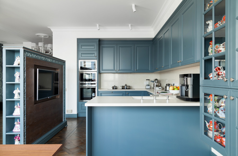 Photo of a traditional u-shaped open plan kitchen in Moscow with an undermount sink, raised-panel cabinets, blue cabinets, white splashback, stainless steel appliances, dark hardwood floors and a peninsula.