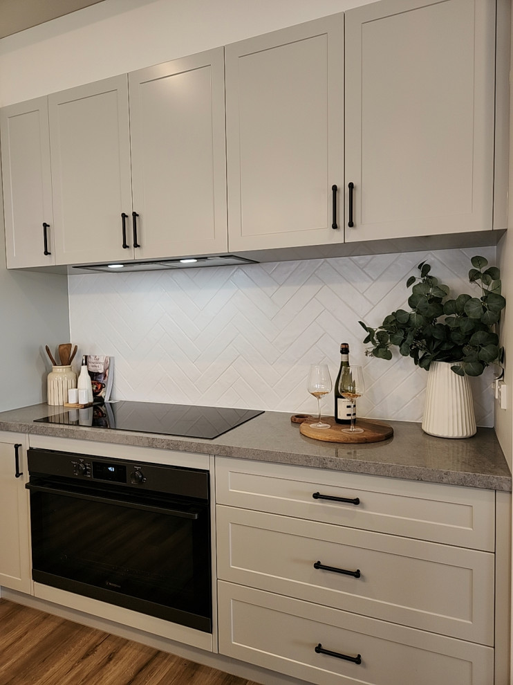 This is an example of a country single-wall kitchen pantry in Melbourne with a farmhouse sink, shaker cabinets, grey cabinets, granite benchtops, white splashback, ceramic splashback, black appliances, laminate floors, beige floor, grey benchtop and vaulted.