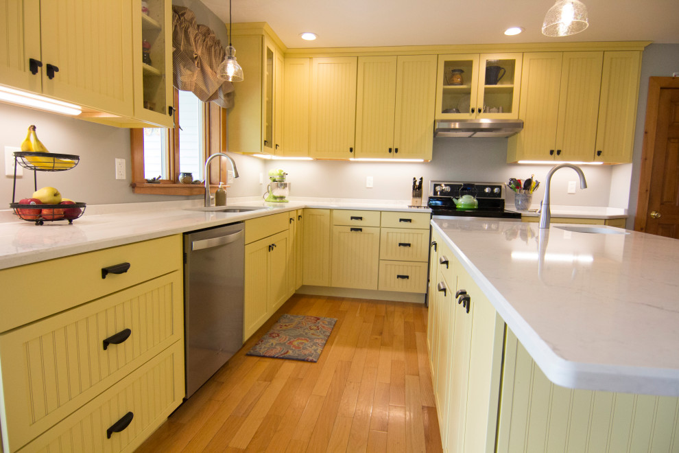 Mid-sized country l-shaped eat-in kitchen in Providence with an undermount sink, recessed-panel cabinets, yellow cabinets, quartz benchtops, grey splashback, stainless steel appliances, light hardwood floors, with island, orange floor and white benchtop.