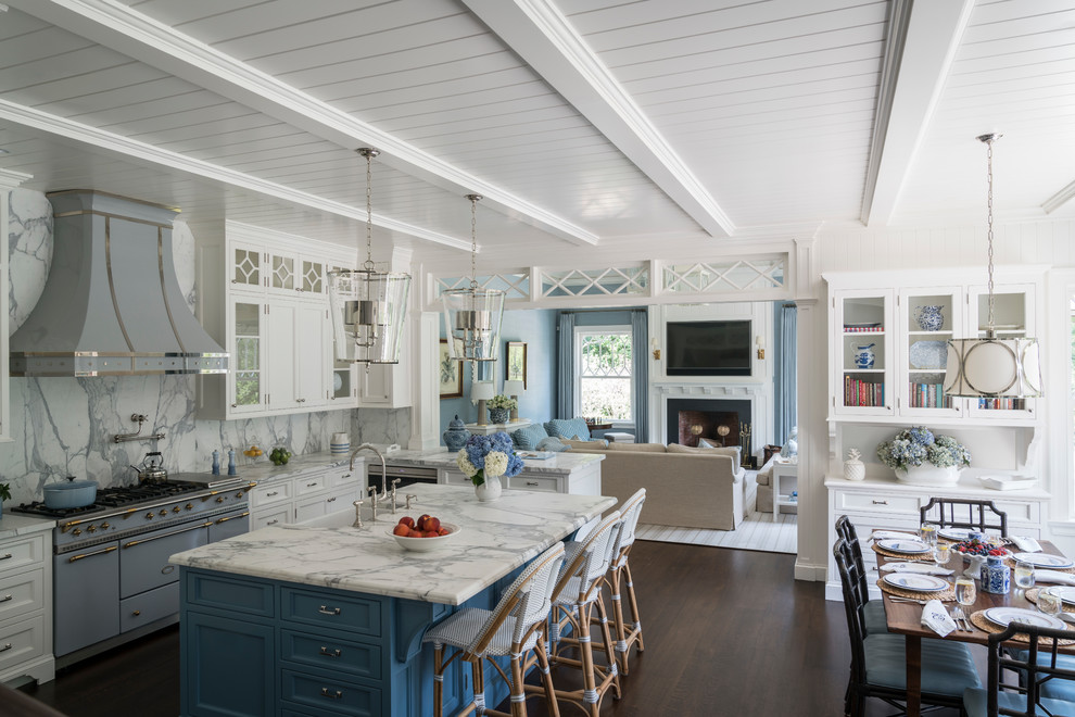 Expansive beach style u-shaped eat-in kitchen in New York with a farmhouse sink, glass-front cabinets, white cabinets, marble benchtops, white splashback, marble splashback, coloured appliances, dark hardwood floors, with island and brown floor.