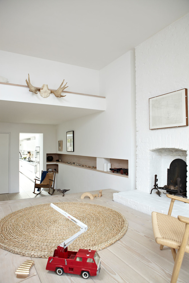 This is an example of a scandinavian open concept living room in London with white walls, light hardwood floors, a standard fireplace, a brick fireplace surround and no tv.