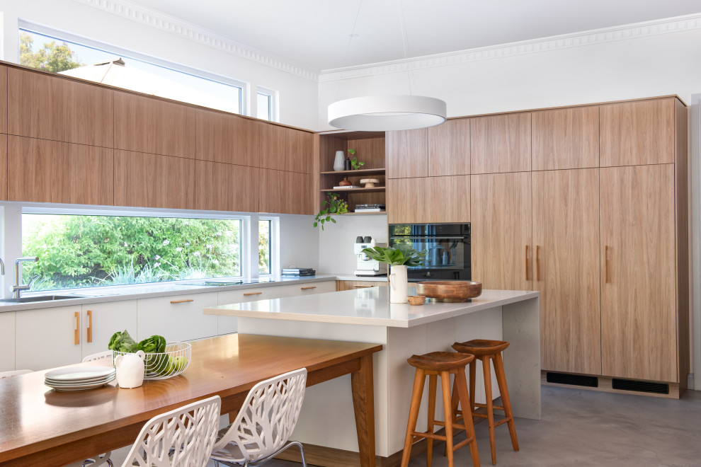 This is an example of a mid-sized contemporary l-shaped eat-in kitchen in Perth with medium wood cabinets, quartz benchtops, white splashback, black appliances, concrete floors, with island and white benchtop.