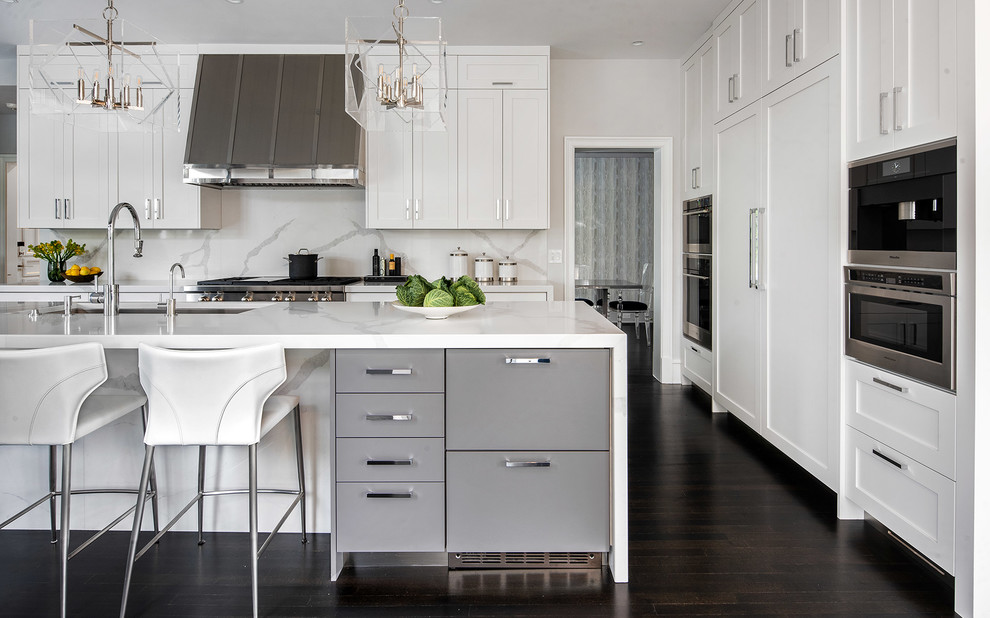 Example of a transitional l-shaped dark wood floor and black floor kitchen design in New York with an undermount sink, shaker cabinets, white cabinets, white backsplash, paneled appliances, an island and white countertops