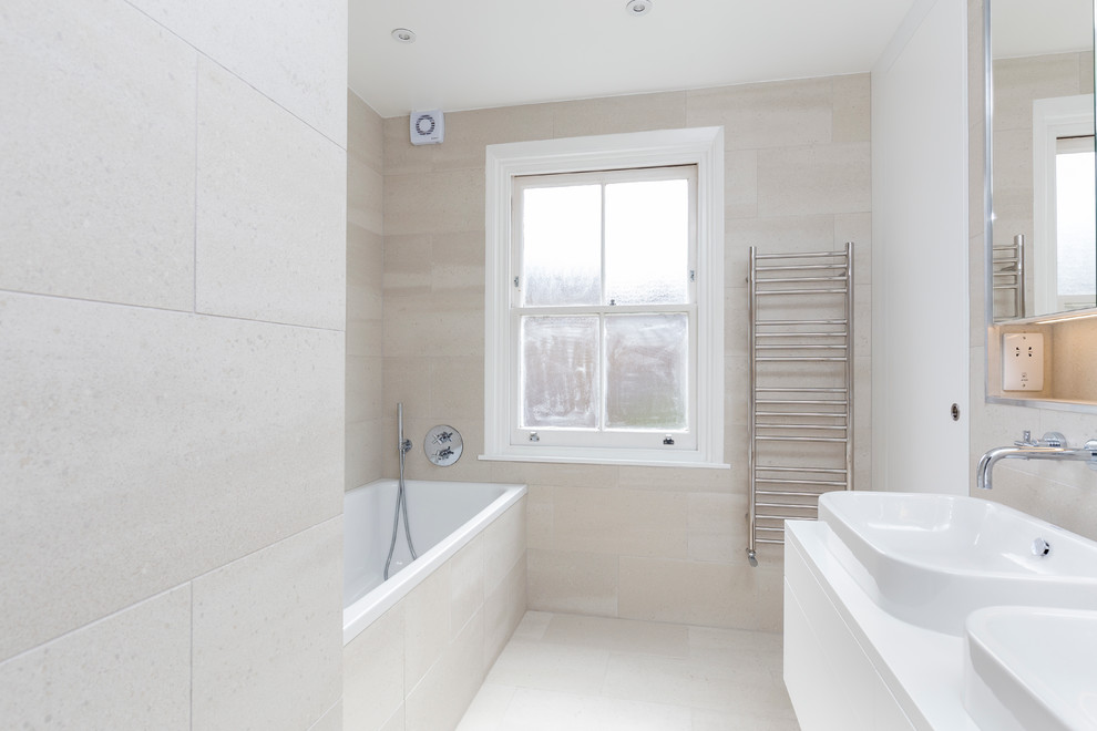 This is an example of a small contemporary kids bathroom in London with flat-panel cabinets, white cabinets, a drop-in tub, an open shower, a wall-mount toilet, beige tile, porcelain tile, beige walls, porcelain floors, a drop-in sink, quartzite benchtops, beige floor and a sliding shower screen.