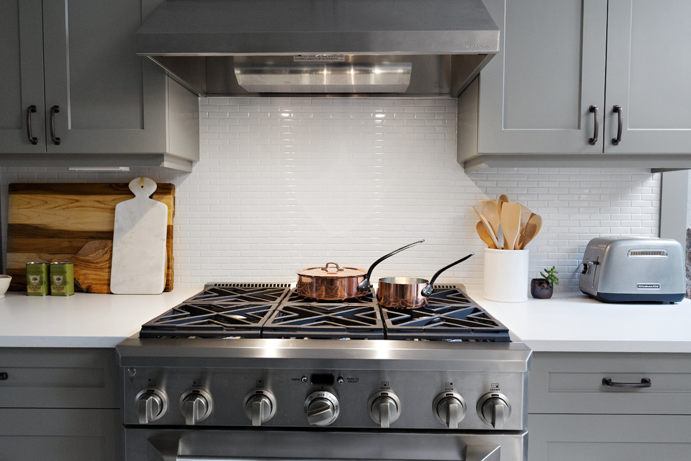 Large transitional l-shaped dark wood floor and brown floor enclosed kitchen photo in Toronto with a farmhouse sink, shaker cabinets, gray cabinets, quartz countertops, white backsplash, porcelain backsplash, stainless steel appliances and no island