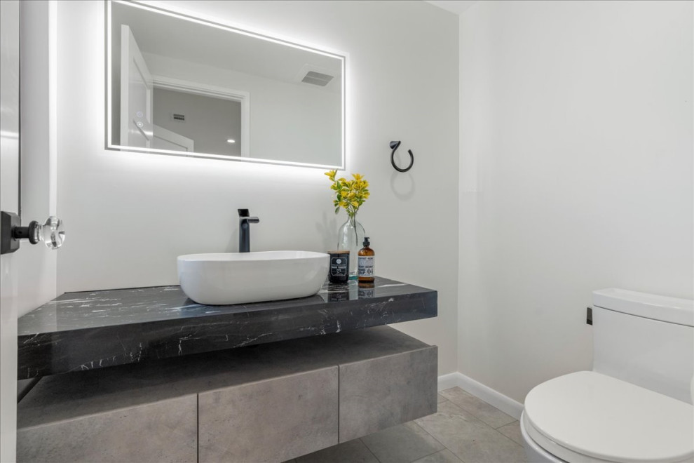 Inspiration for a large beach style bathroom in San Francisco with flat-panel cabinets, grey cabinets, a two-piece toilet, white tile, white walls, vinyl floors, a vessel sink, solid surface benchtops, grey floor, black benchtops, a single vanity and a floating vanity.