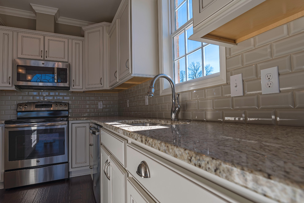 Inspiration for a mid-sized transitional l-shaped dark wood floor open concept kitchen remodel with an undermount sink, recessed-panel cabinets, white cabinets, granite countertops, gray backsplash, subway tile backsplash, stainless steel appliances and an island