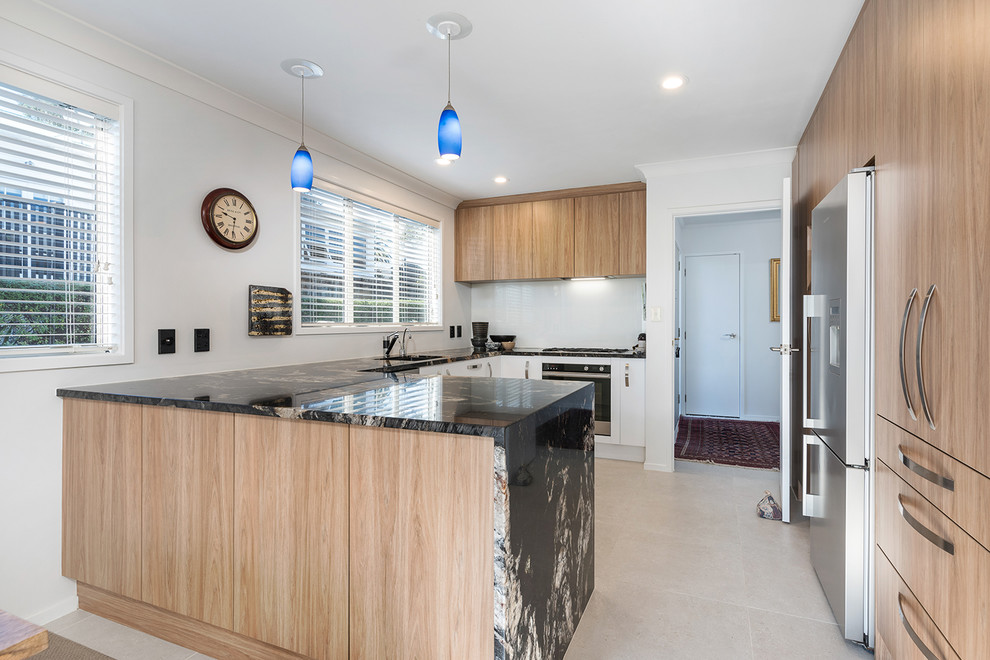 Mid-sized contemporary u-shaped eat-in kitchen in Auckland with flat-panel cabinets, a peninsula, granite benchtops, an undermount sink, grey splashback, glass sheet splashback, stainless steel appliances, ceramic floors and beige floor.
