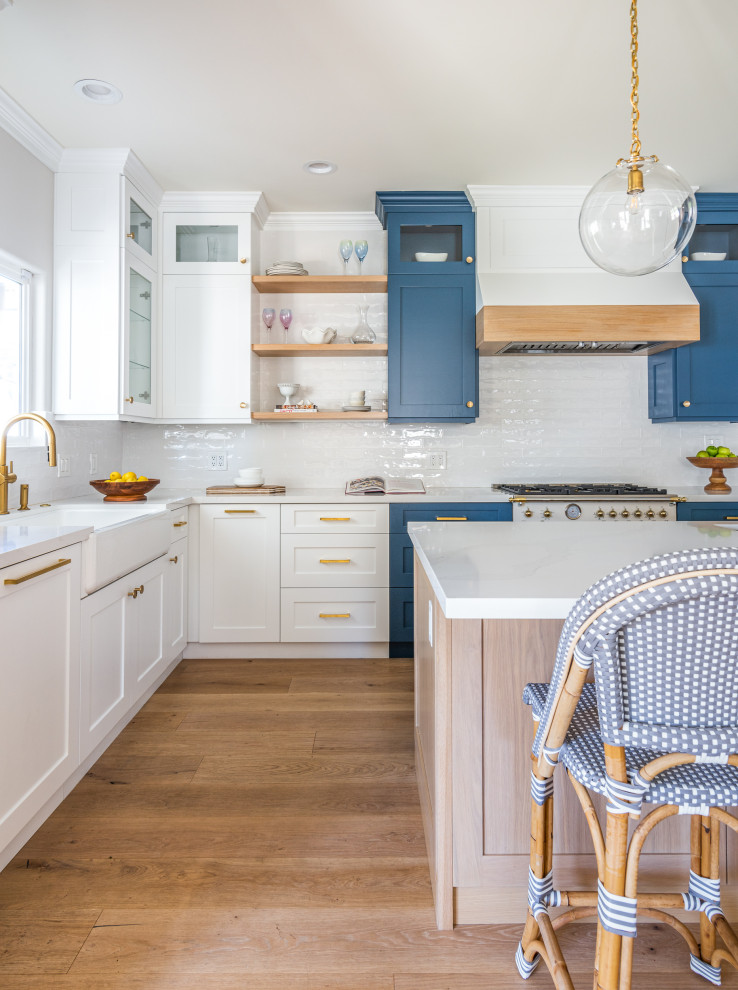 Inspiration for a mid-sized coastal u-shaped light wood floor open concept kitchen remodel in Los Angeles with a farmhouse sink, shaker cabinets, white cabinets, quartz countertops, white backsplash, subway tile backsplash, an island and white countertops