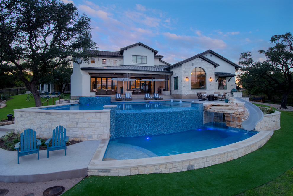 Photo of a large mediterranean backyard custom-shaped infinity pool in Austin with a water slide and concrete pavers.