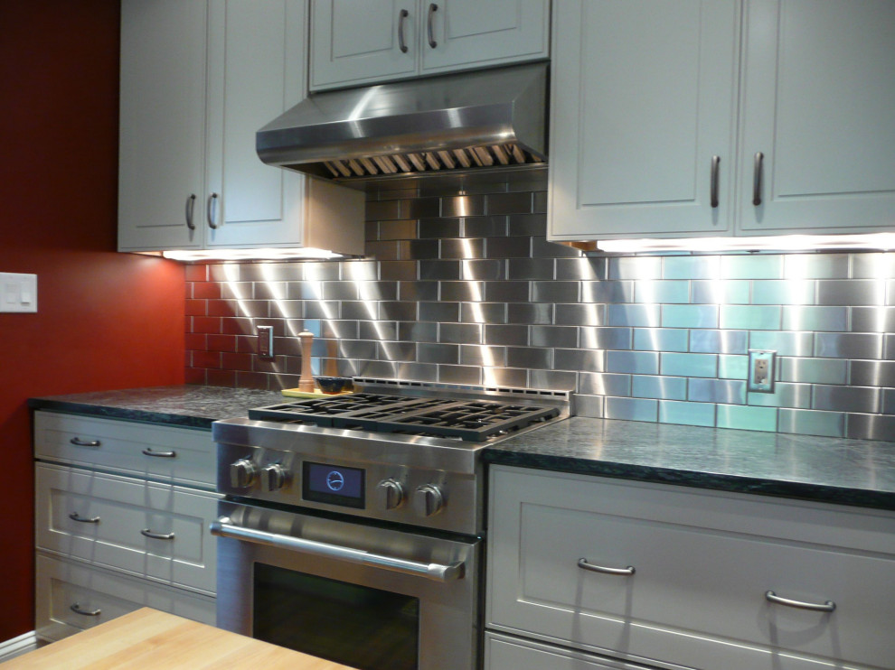 This is an example of a traditional kitchen in New York with white cabinets, metal splashback, stainless steel appliances, a submerged sink, raised-panel cabinets and metallic splashback.