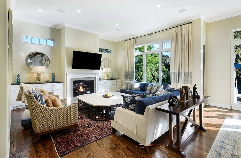 Expansive arts and crafts open concept family room in Los Angeles with beige walls, painted wood floors, a standard fireplace, a wood fireplace surround, a wall-mounted tv and brown floor.