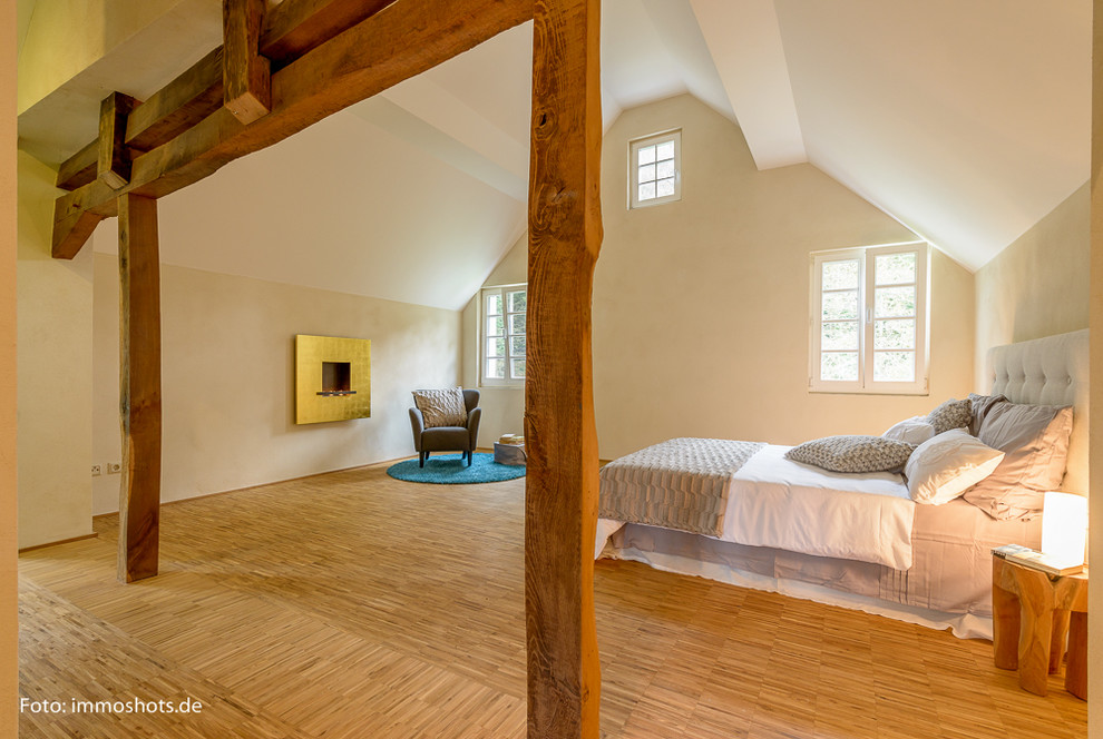 This is an example of an expansive country bedroom in Cologne with beige walls, medium hardwood floors and a standard fireplace.