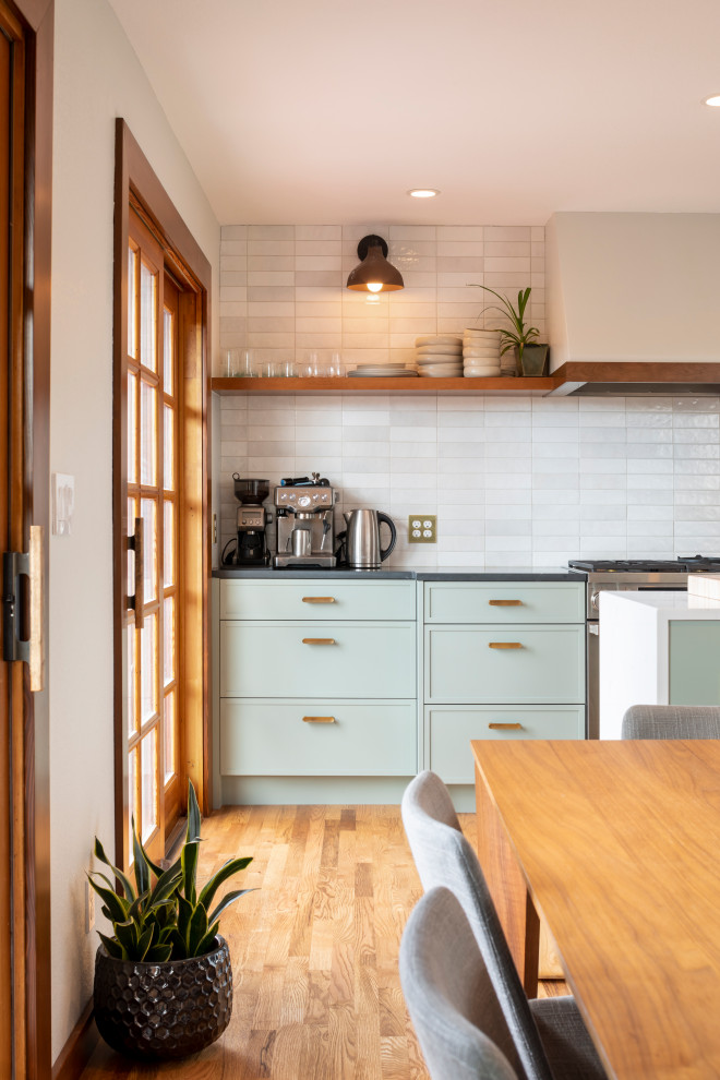 Photo of a medium sized contemporary single-wall open plan kitchen in Seattle with a belfast sink, shaker cabinets, green cabinets, engineered stone countertops, white splashback, ceramic splashback, stainless steel appliances, medium hardwood flooring, an island and white worktops.