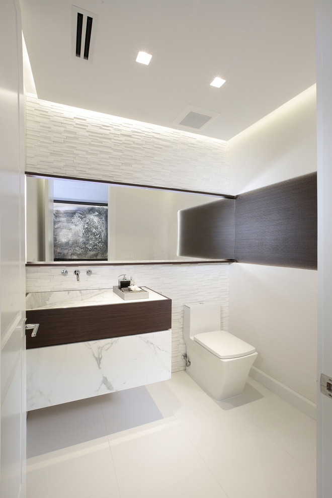 This is an example of a contemporary powder room in Miami with flat-panel cabinets, a one-piece toilet, white tile, stone tile and white walls.