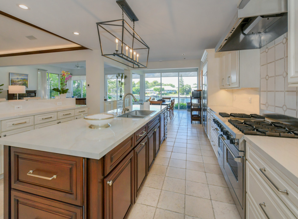 Large transitional galley travertine floor and beige floor eat-in kitchen photo with a double-bowl sink, recessed-panel cabinets, white cabinets, beige backsplash, porcelain backsplash, stainless steel appliances, an island and white countertops