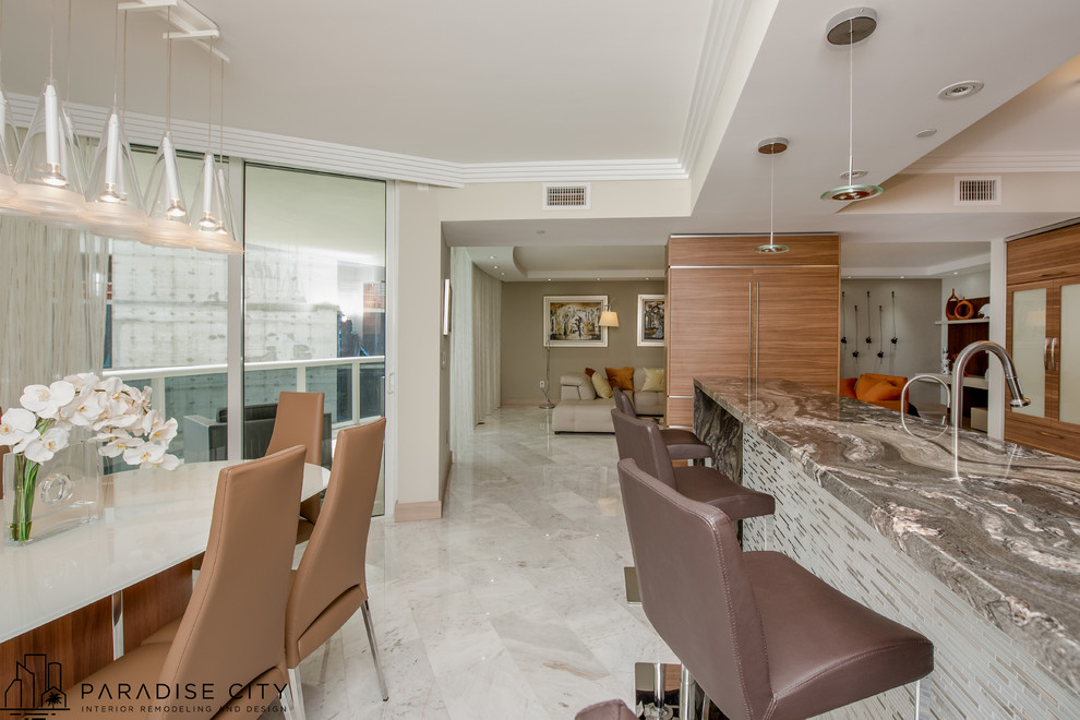 Photo of a mid-sized contemporary l-shaped eat-in kitchen in Miami with a drop-in sink, flat-panel cabinets, light wood cabinets, granite benchtops, grey splashback, mosaic tile splashback, stainless steel appliances, marble floors and with island.