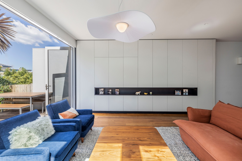 Medium sized modern open plan living room in Sydney with white walls, medium hardwood flooring, a built-in media unit and brown floors.
