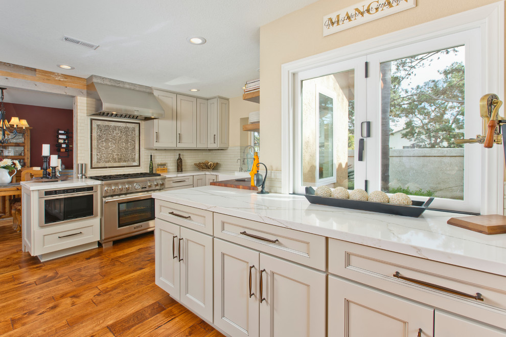 Example of a mid-sized transitional u-shaped medium tone wood floor open concept kitchen design in Tampa with a farmhouse sink, recessed-panel cabinets, gray cabinets, quartzite countertops, beige backsplash, porcelain backsplash, stainless steel appliances and no island