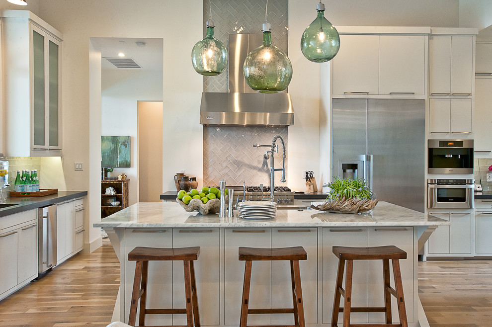 This is an example of a transitional kitchen in Austin with flat-panel cabinets, stainless steel appliances, marble benchtops, white cabinets, grey splashback and glass tile splashback.