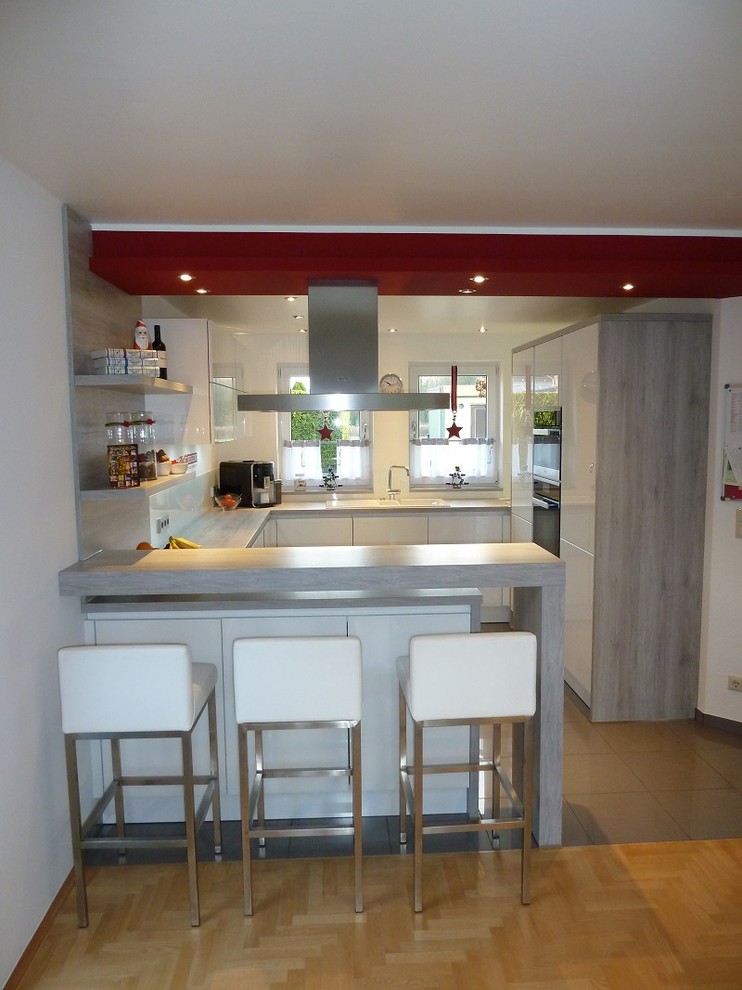 This is an example of a mid-sized contemporary u-shaped open plan kitchen in Hamburg with flat-panel cabinets, white cabinets and white splashback.