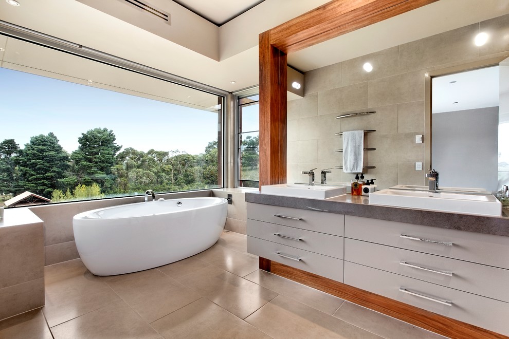 Photo of a large contemporary bathroom in Melbourne with a drop-in sink, flat-panel cabinets, grey cabinets, engineered quartz benchtops, a freestanding tub, gray tile, porcelain tile, grey walls and porcelain floors.