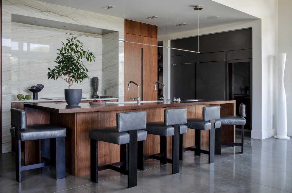 Example of a large minimalist concrete floor and gray floor eat-in kitchen design in Denver with a farmhouse sink, flat-panel cabinets, dark wood cabinets, slate backsplash, paneled appliances and an island