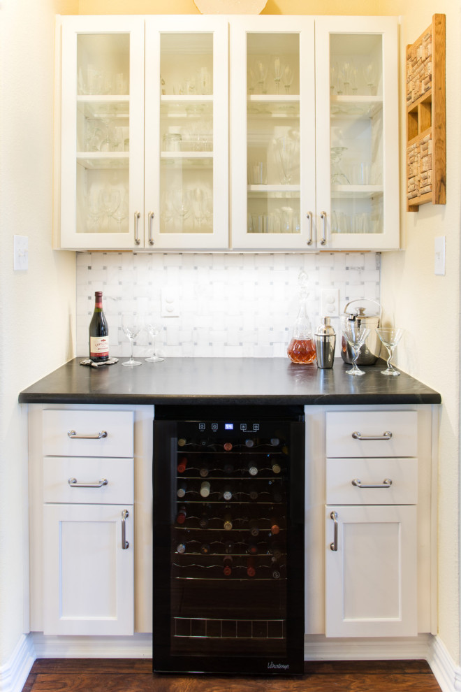 Photo of a small eclectic galley home bar in Dallas with glass-front cabinets, white cabinets, soapstone benchtops and black benchtop.