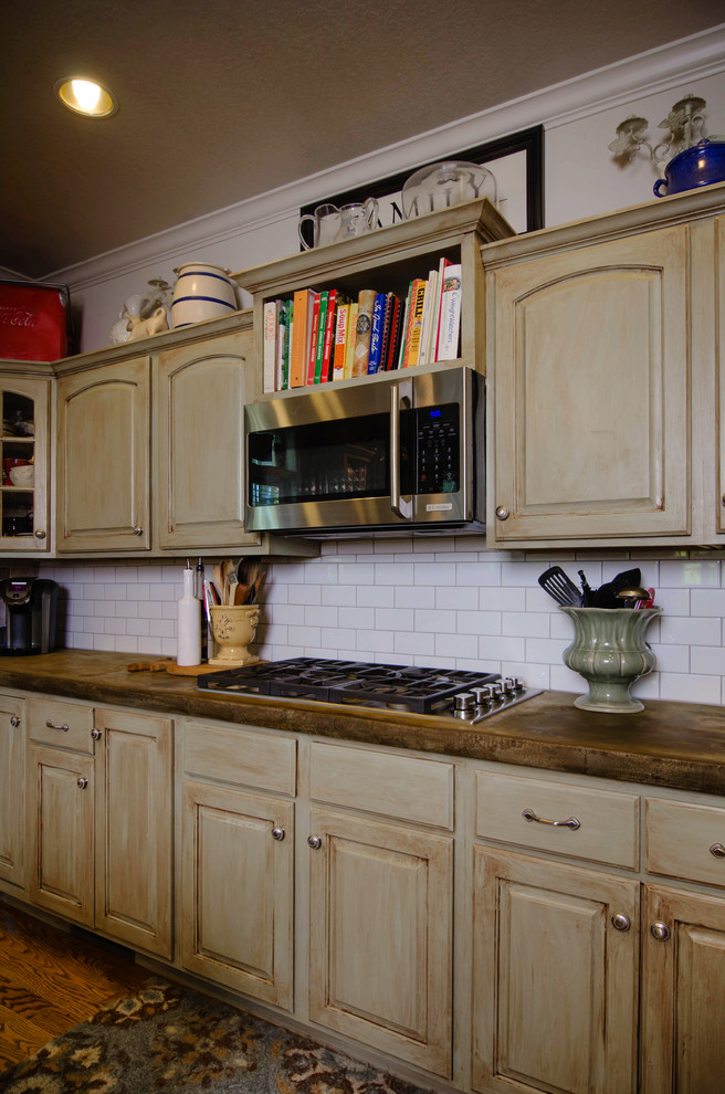 Inspiration for a mid-sized traditional u-shaped kitchen in Other with a farmhouse sink, distressed cabinets, concrete benchtops, white splashback, subway tile splashback, stainless steel appliances, medium hardwood floors, with island and raised-panel cabinets.