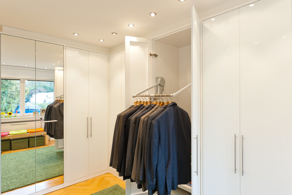 Photo of a mid-sized contemporary gender-neutral storage and wardrobe in Essen with flat-panel cabinets, white cabinets and light hardwood floors.