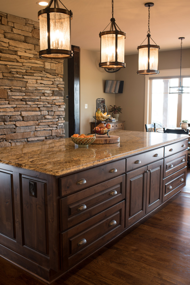 Example of a large mountain style l-shaped dark wood floor and brown floor eat-in kitchen design with a farmhouse sink, raised-panel cabinets, dark wood cabinets, granite countertops, gray backsplash, ceramic backsplash, black appliances and an island