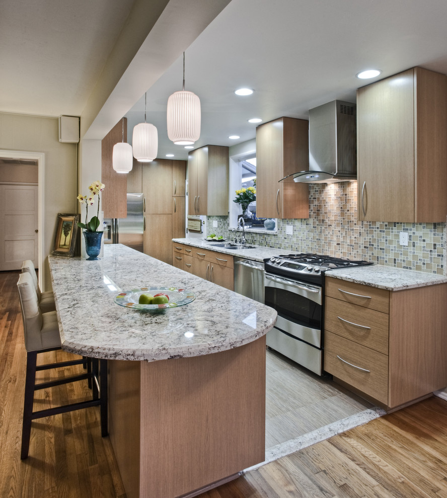 Photo of a mid-sized traditional galley open plan kitchen in Los Angeles with an undermount sink, flat-panel cabinets, light wood cabinets, granite benchtops, multi-coloured splashback, stainless steel appliances, with island and light hardwood floors.