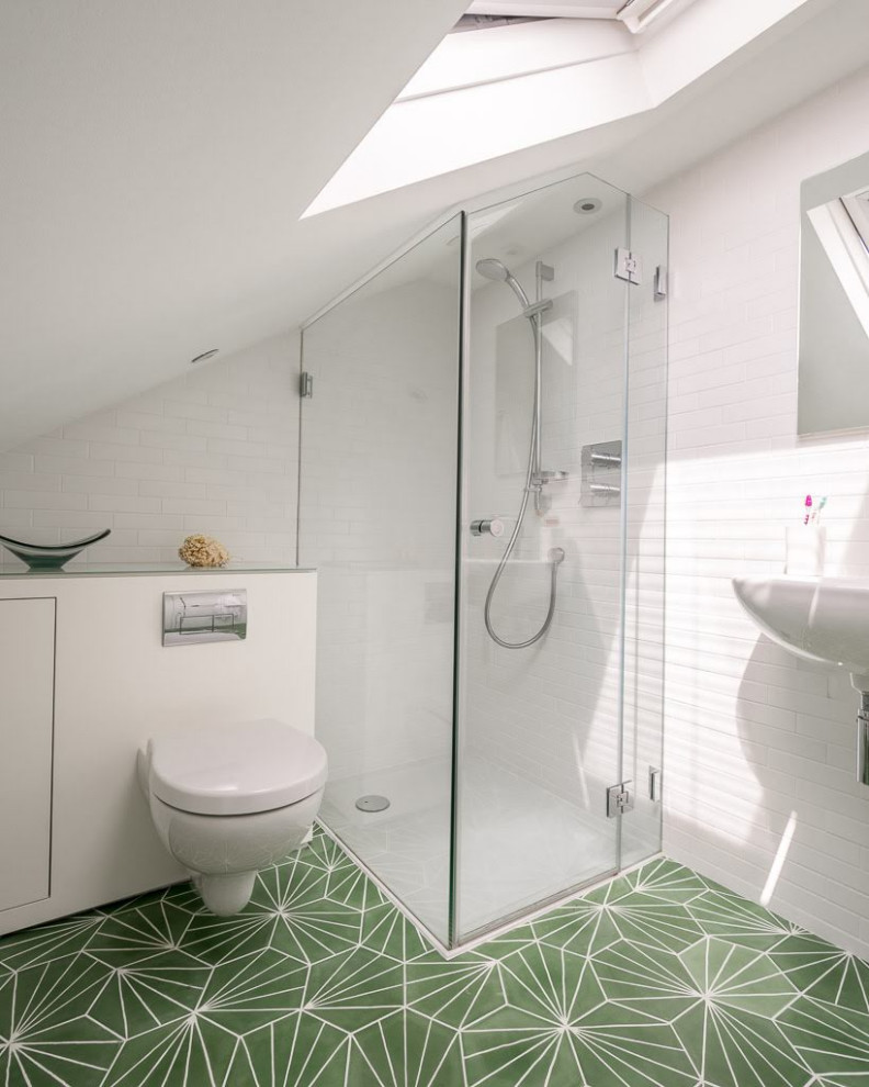 Small contemporary master bathroom in London with flat-panel cabinets, white cabinets, a corner shower, a wall-mount toilet, white tile, ceramic tile, white walls, cement tiles, a wall-mount sink, glass benchtops, green floor, a hinged shower door, white benchtops, a laundry, a single vanity, a floating vanity and vaulted.