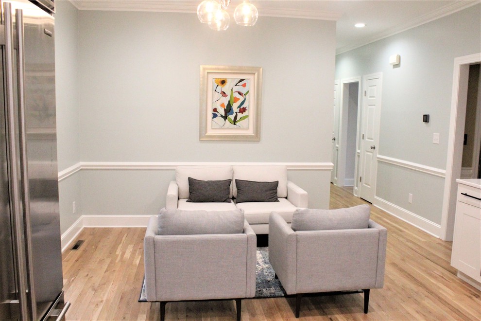 Example of a large transitional galley light wood floor eat-in kitchen design with a farmhouse sink, shaker cabinets, white cabinets, quartz countertops, white backsplash, ceramic backsplash, stainless steel appliances, an island and white countertops