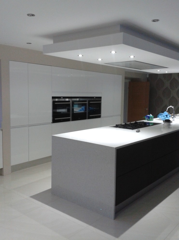This is an example of a mid-sized contemporary galley open plan kitchen in Berkshire with an integrated sink, flat-panel cabinets, white cabinets, solid surface benchtops, stainless steel appliances, porcelain floors and with island.