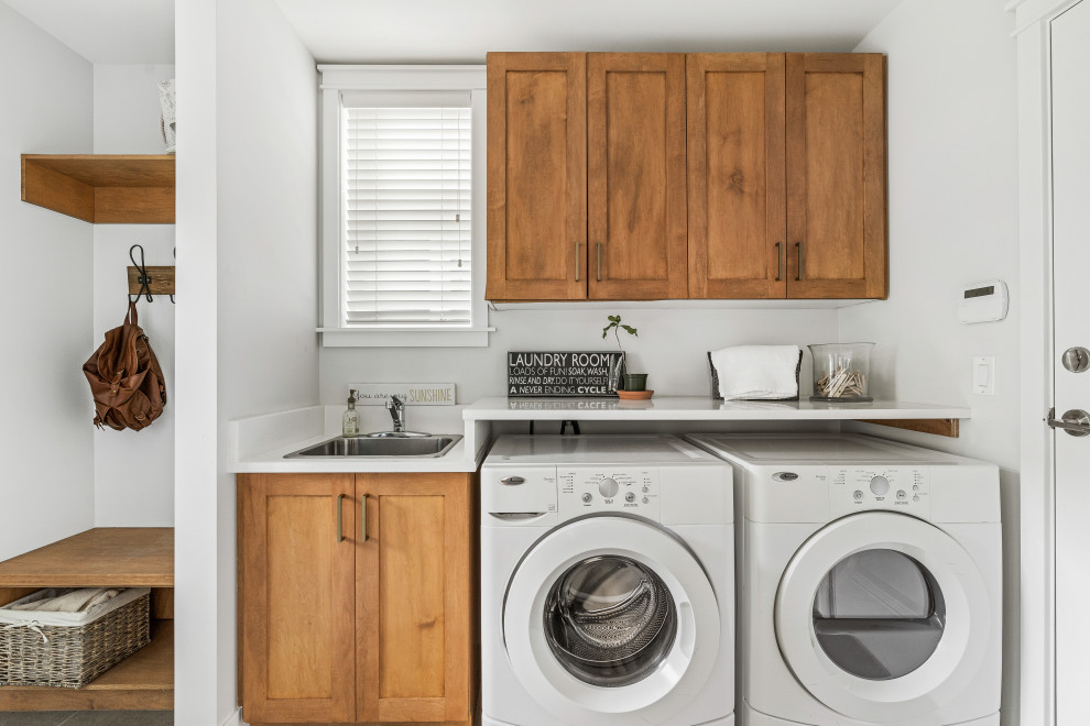 Design ideas for a transitional dedicated laundry room in Vancouver with a drop-in sink, shaker cabinets, medium wood cabinets, white walls, a side-by-side washer and dryer and white benchtop.