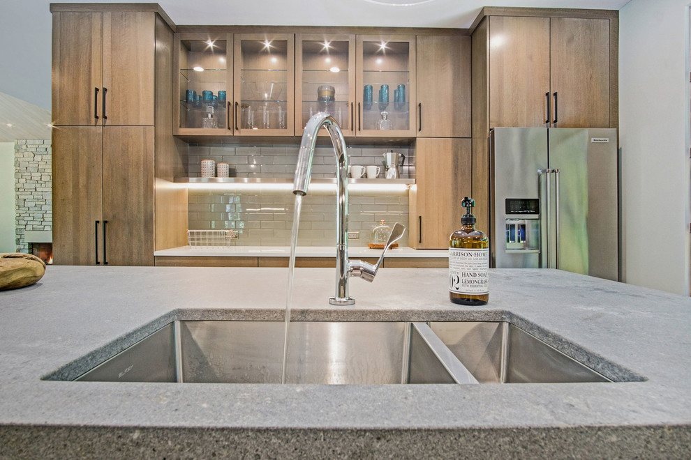 Inspiration for a rustic medium tone wood floor kitchen remodel in Grand Rapids with an undermount sink, flat-panel cabinets, quartz countertops, green backsplash, glass tile backsplash and stainless steel appliances