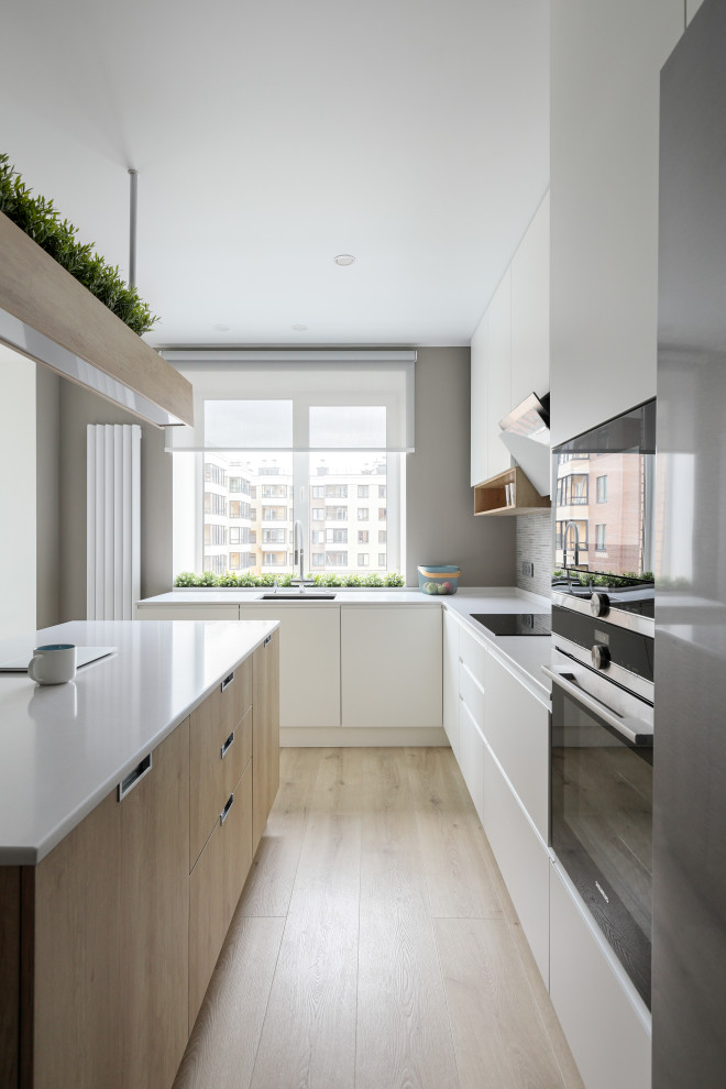 Mid-sized scandinavian u-shaped eat-in kitchen in Saint Petersburg with a single-bowl sink, flat-panel cabinets, white cabinets, solid surface benchtops, beige splashback, ceramic splashback, black appliances, medium hardwood floors, with island, brown floor and white benchtop.
