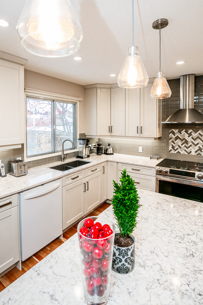Example of a large transitional u-shaped medium tone wood floor eat-in kitchen design in Calgary with an undermount sink, shaker cabinets, white cabinets, gray backsplash, glass tile backsplash, stainless steel appliances, an island and marble countertops
