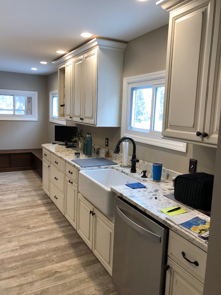This is an example of a small traditional galley separate kitchen in Burlington with a farmhouse sink, raised-panel cabinets, distressed cabinets, stainless steel appliances, no island, grey floor and white benchtop.