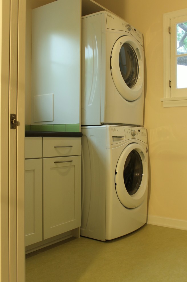 This is an example of a small eclectic galley dedicated laundry room in Los Angeles with shaker cabinets, white cabinets, quartz benchtops, linoleum floors, a stacked washer and dryer and beige walls.