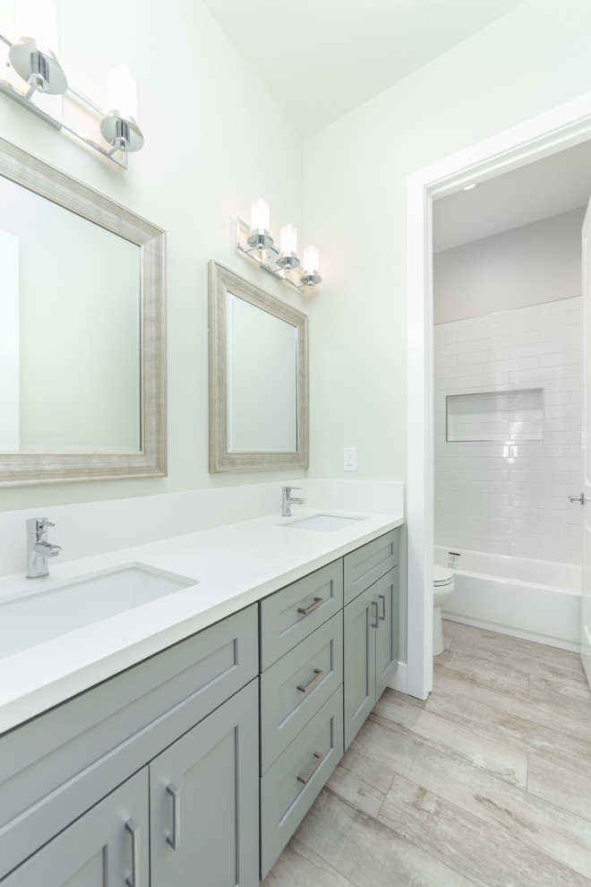 Mid-sized contemporary kids bathroom in Sacramento with flat-panel cabinets, grey cabinets, a freestanding tub, a corner shower, a one-piece toilet, white walls, medium hardwood floors, an integrated sink, granite benchtops, beige floor, a hinged shower door and white benchtops.